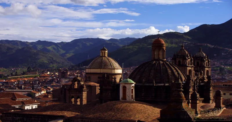 The domes of Cusco Cathedral above the rooftops, with the mountains behind.